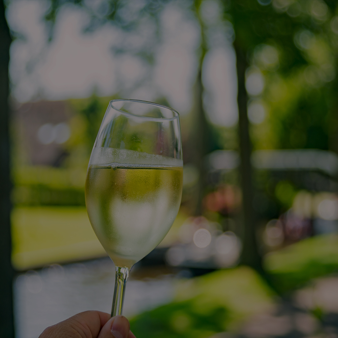 A glass of sparkling wine held up against a blurred canal-side backdrop